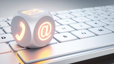 © www.istock.com/peterschreiber.media Ein Würfel mit dem ad-Zeichen, einem Telefonhörer und einem Briefumschlag auf einer Tastatur sind zu sehen.