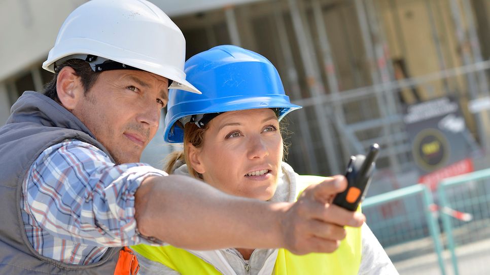 © https://stock.adobe.com/de Das Bild zeigt zwei Personen mit Bauhelmen, die in eine gemeinsame Richtung sehen.