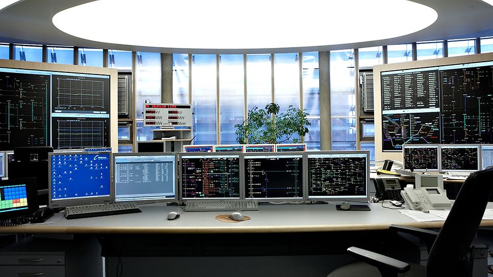 Ein Kontrollraum mit mehreren Computermonitoren, Tastaturen und Telefonen auf einem Schreibtisch.