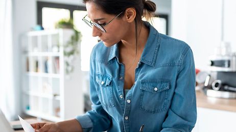 Eine Frau prüft ein Dokument in einer Küche mit einem Laptop
