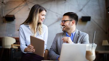 Zwei Personen arbeiten gemeinsam an Laptop und Tablet in einem modernen Besprechungsraum.