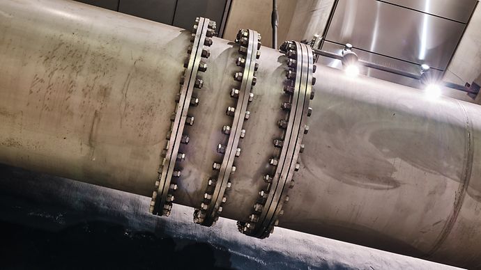 Großes Metallrohr mit mehreren Flanschen und Schraubverbindungen in einer beleuchteten Anlage