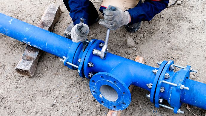 Person zieht Schrauben an einer blauen Wasserleitung fest