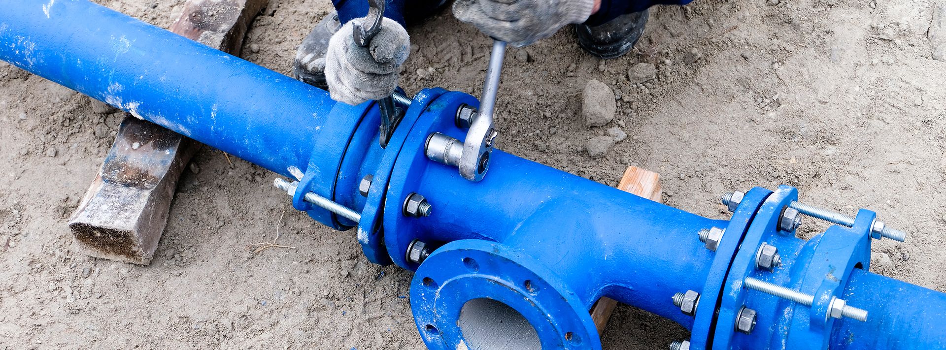 Person zieht Schrauben an einer blauen Wasserleitung fest