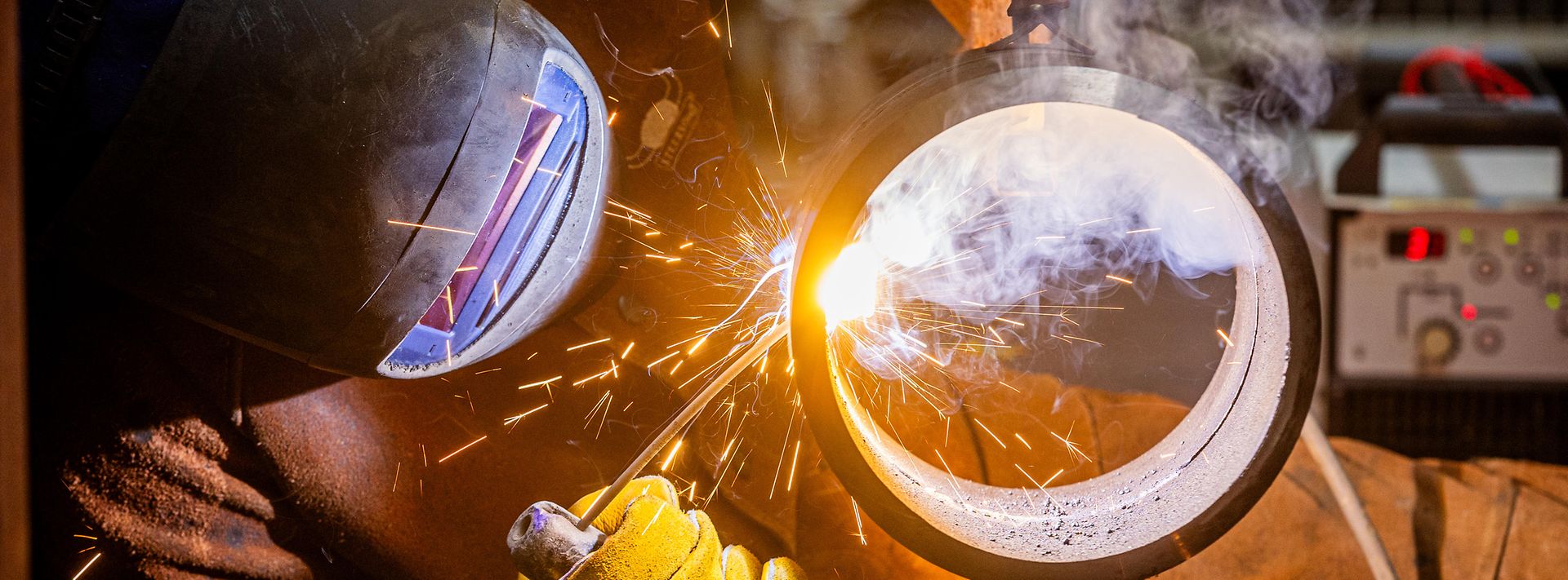 Eine Person mit Arbeitskleidung und Schutzhelm schweißt