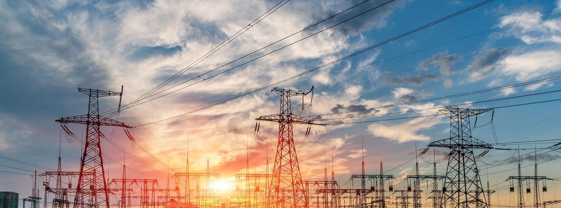 Eine große Stromtrassen- und Umspannwerksanlage vor einem farbenprächtigen Sonnenuntergang mit zahlreichen Hochspannungsmasten.
