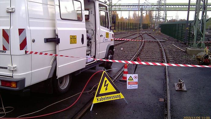 Abgesperrte Kabelmessung an Bahngleisen mit Servicefahrzeug und Warnschild.