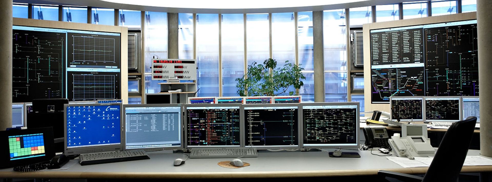 Ein Kontrollraum mit mehreren Computermonitoren, Tastaturen und Telefonen auf einem Schreibtisch.