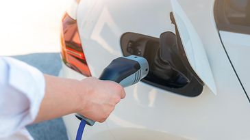 Eine Person steckt ein Ladekabel in ein Elektroauto
